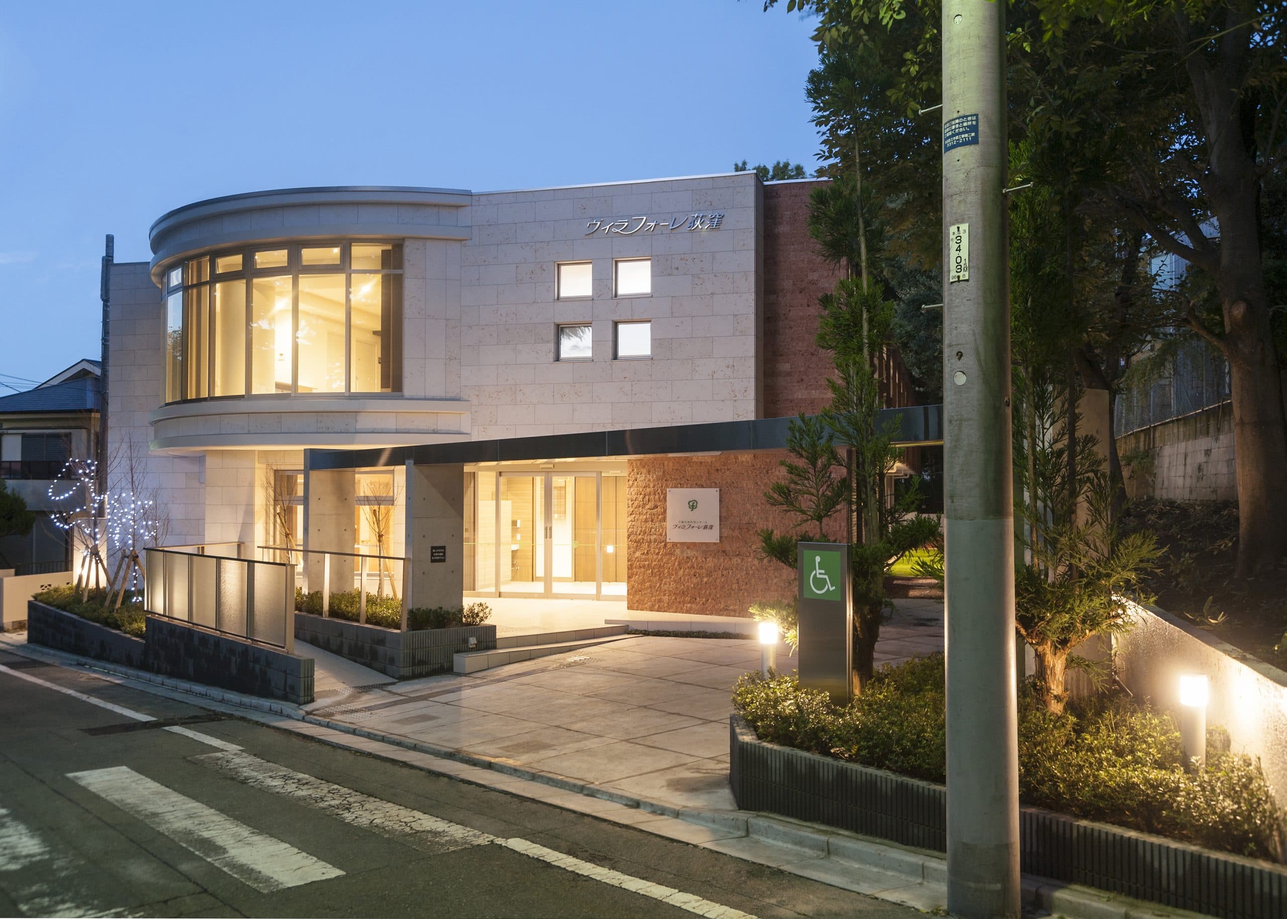 夕暮れのヴィラフォーレ荻窪。曲面の大きなガラス窓に明かりがともる白い地上2階建ての建物